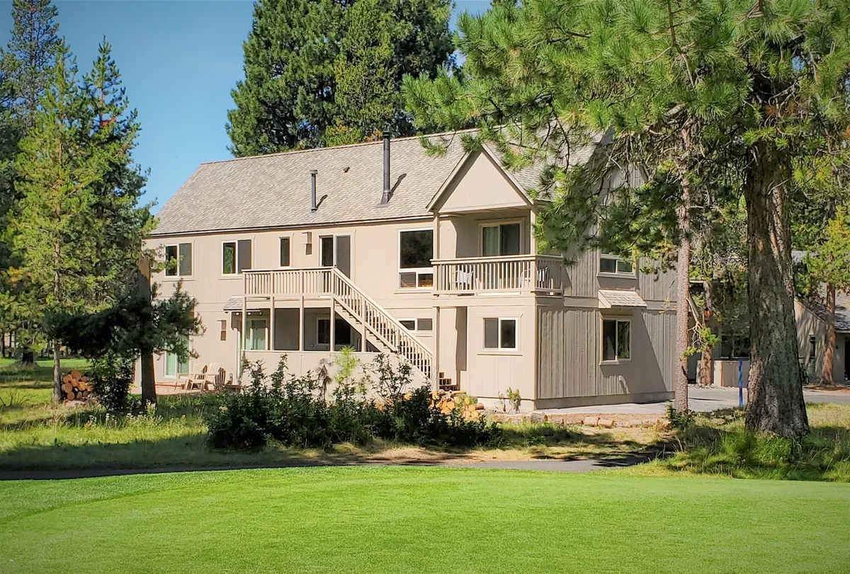 A two-story house with a balcony, surrounded by lush trees, with a staircase leading to a spacious lawn. The balcony offers elevated views, hinting at the sweeping perspectives available from the home.