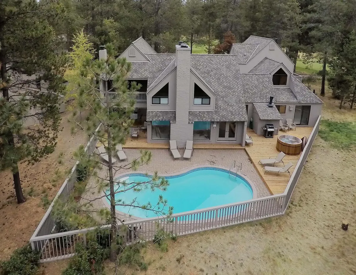 A beautiful exterior shot of the home’s private heated swimming pool and spacious hot tub, surrounded by a wooden deck and tall trees, with the house and natural landscape in the background. Comfortable deck seating and poolside areas are visible, accentuating the inviting, resort-style outdoor amenities.