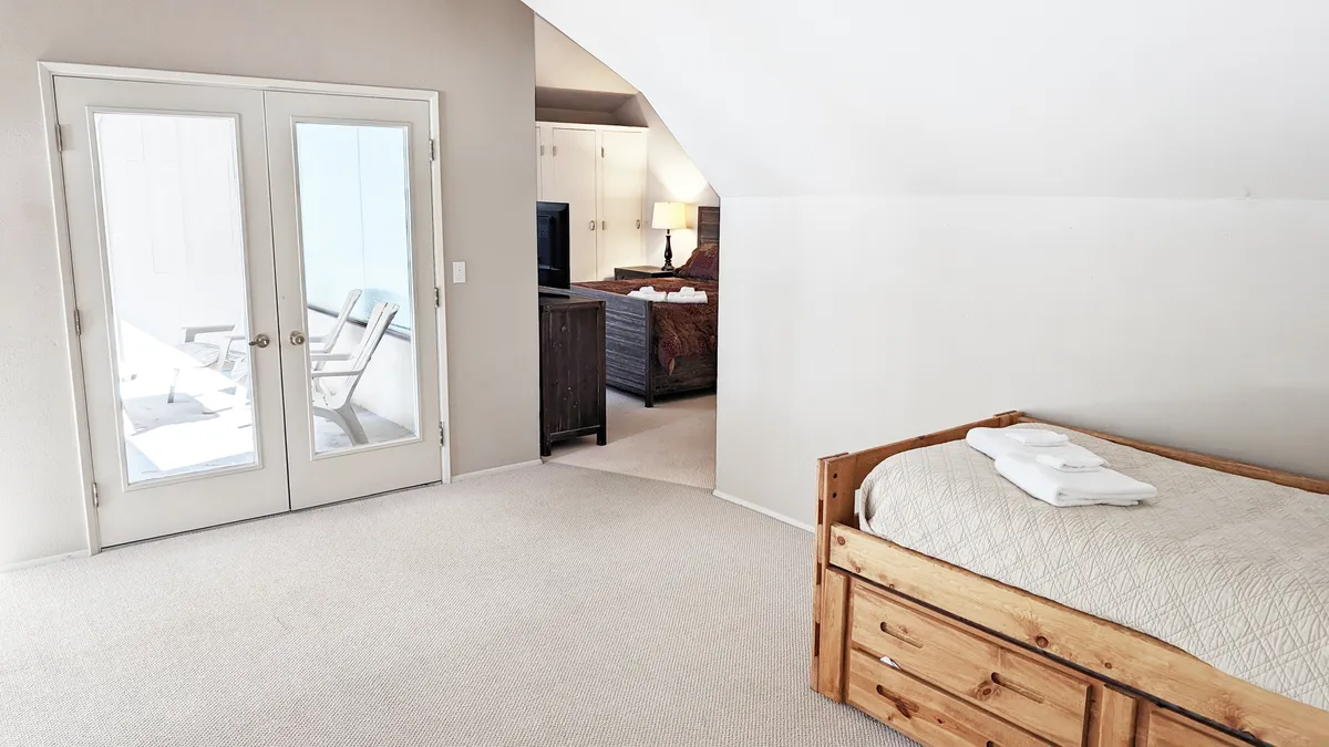 A peaceful bedroom with a bed facing double doors that open to the outside. A cozy seating area completes the scene, suggesting flexible spaces for relaxation and direct access to a patio or balcony. The space is bright, calm, and welcoming.