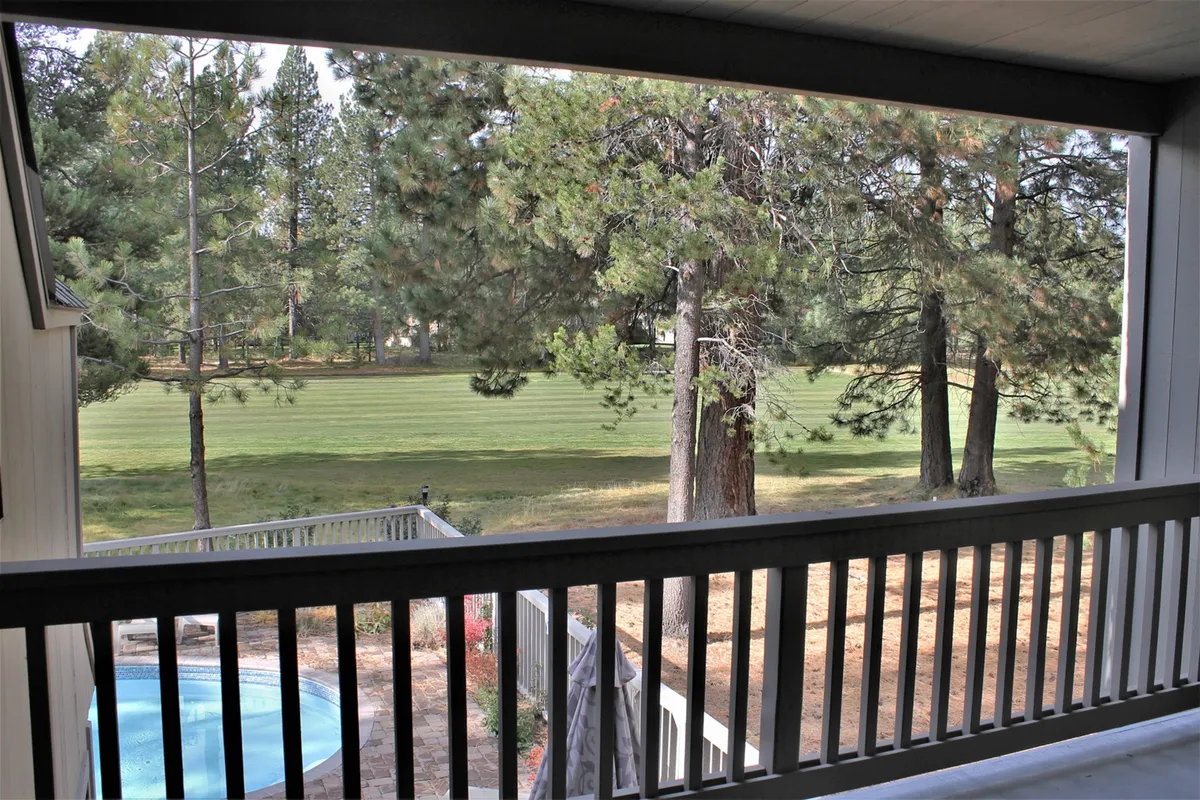 A tranquil outdoor view featuring a green lawn, tall trees, and a deck railing that overlooks a pool. The space invites gatherings, relaxation, and outdoor enjoyment, perfectly suited for group activities and family leisure.