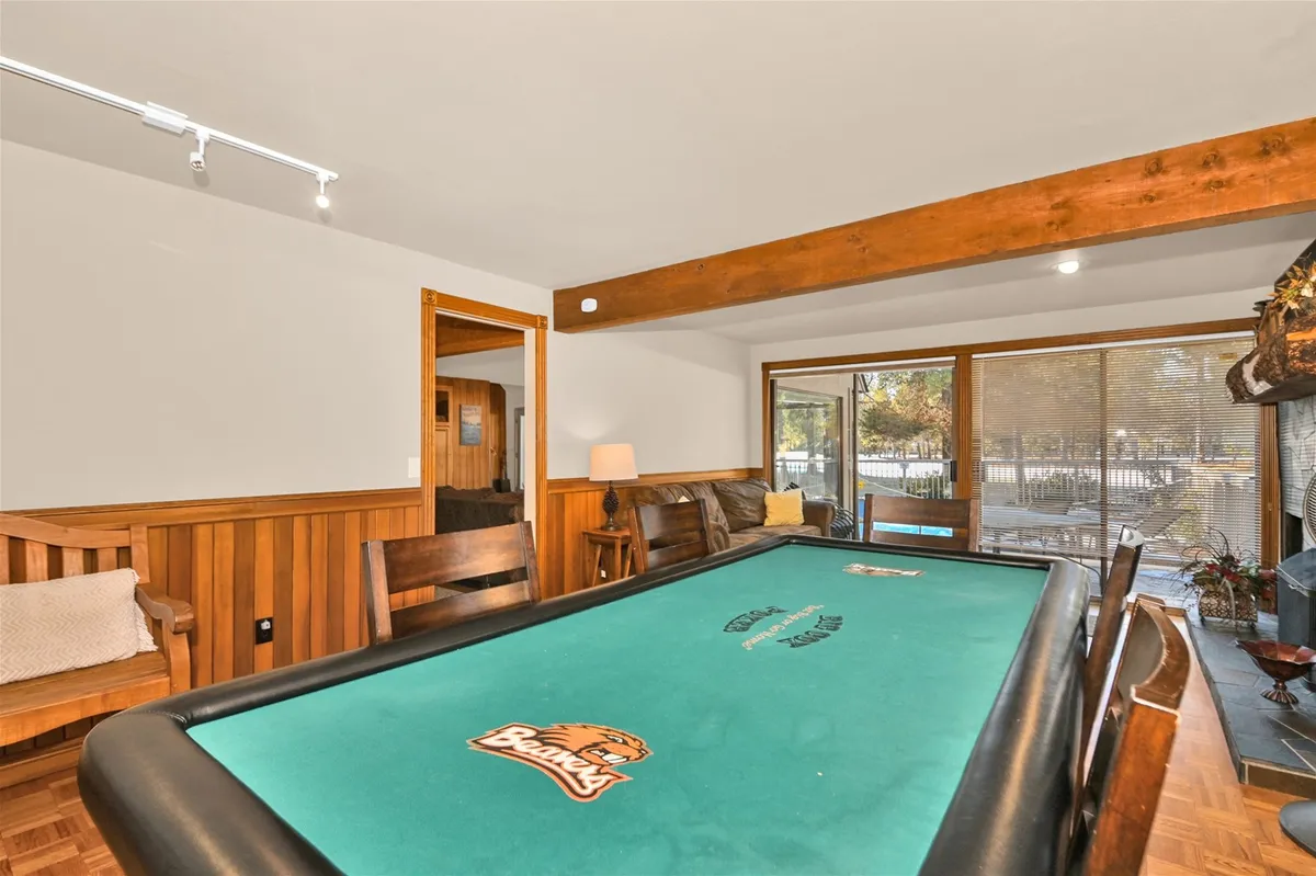 A stylish game room featuring a pool table, striking wooden beams, and large windows that fill the space with light. The design encourages casual socializing, friendly competition, and relaxed hangouts, making it perfect for both day and night gatherings.