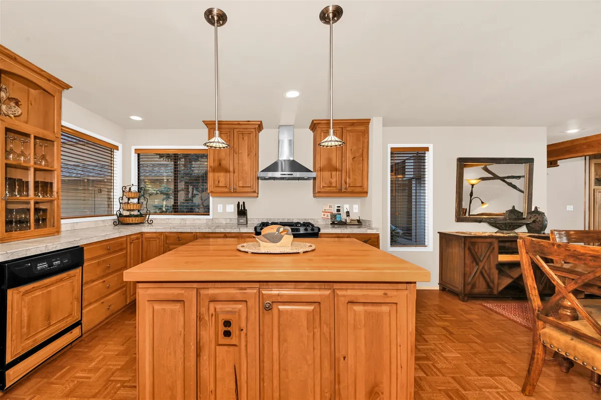 A spacious, warmly lit kitchen featuring a large island, wooden cabinetry, pendant lights, and stainless steel appliances. The setting invites social cooking and group gatherings, with ample space for multiple cooks and guests to interact.
