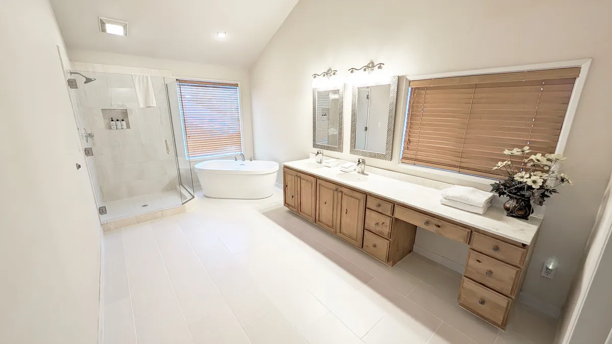 A luxurious spa-style bathroom with a freestanding bathtub, dual sinks, large mirrors, and ample natural light streaming in from windows. The space is modern and calming, perfect for self-care routines and relaxing soaks after a day of activity.