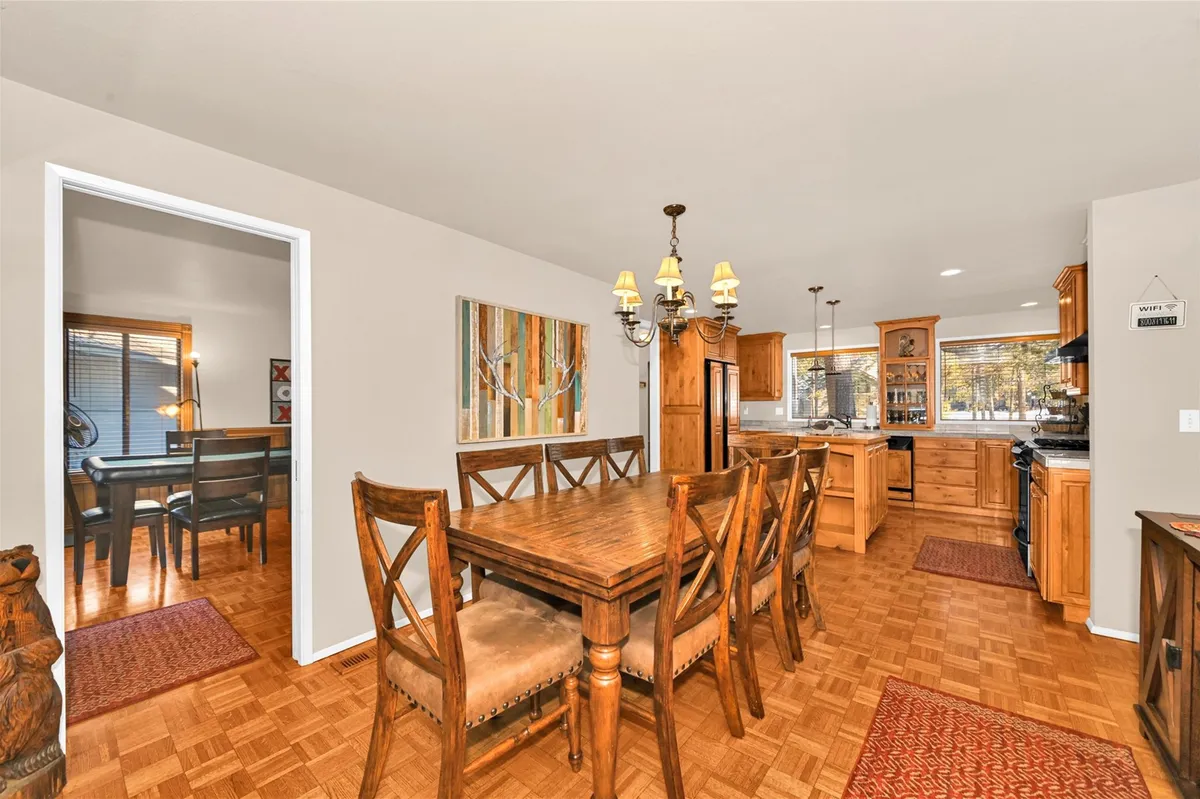 A cheerful dining area adjacent to the kitchen, complete with a large wooden table, elegant chandelier, and inviting decor. The space is ready for family dinners or festive gatherings, with a glimpse of the kitchen in the background.