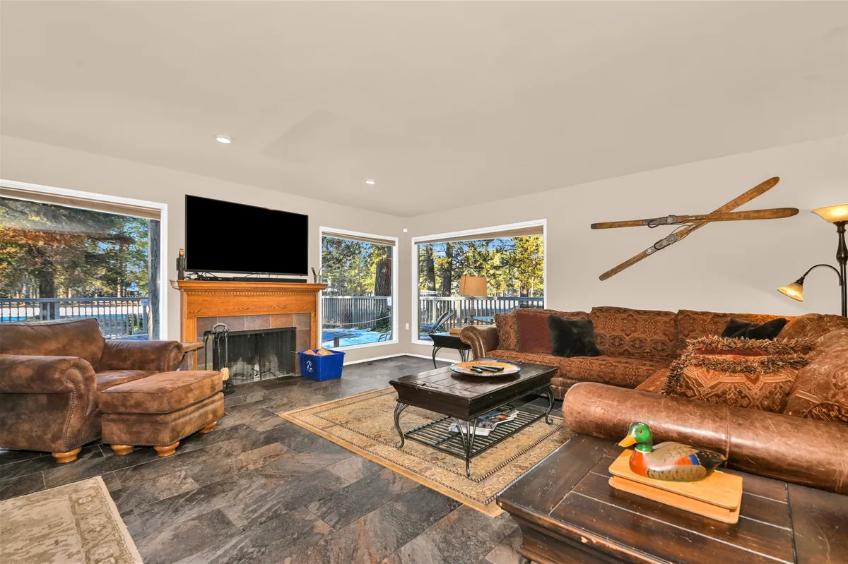 A spacious, sunlit Great Room featuring large windows with panoramic views, a cozy fireplace, plush sofas, and a welcoming coffee table. The atmosphere is warm and inviting, perfect for group relaxation or lively conversation. Decorative items and comfortable furnishings set a stylish yet approachable tone.